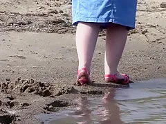 On high heels and bare feet on the sand, plump legs walk along the shore.
